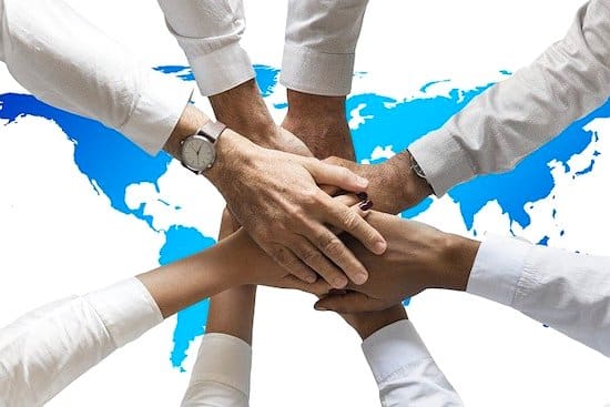 A group of people joining hands, with the map of the world in the background.