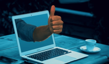 A hand making a thumbs-up gesture through a laptop screen.